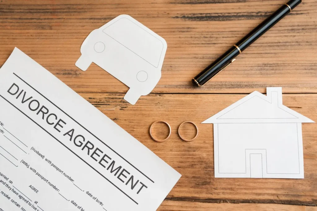 Divorce agreement document with paper cutouts of a car and house, two wedding rings, and a pen on a wooden table, symbolizing family law appeals and asset division.