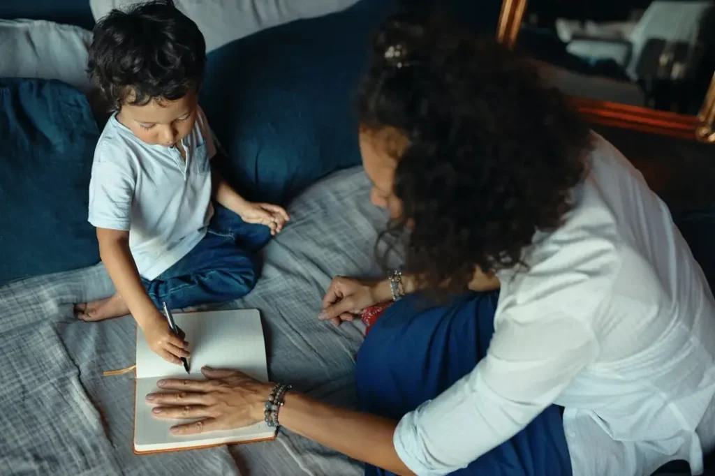 Child writing in notebook with mother assisting, illustrating family interaction and support in a home setting, relevant to family law appeals and custody discussions.