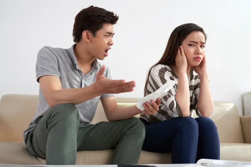 Couple arguing on a couch, man expressing frustration and holding a document, woman showing distress and covering her ears, reflecting family law disputes and emotional challenges.