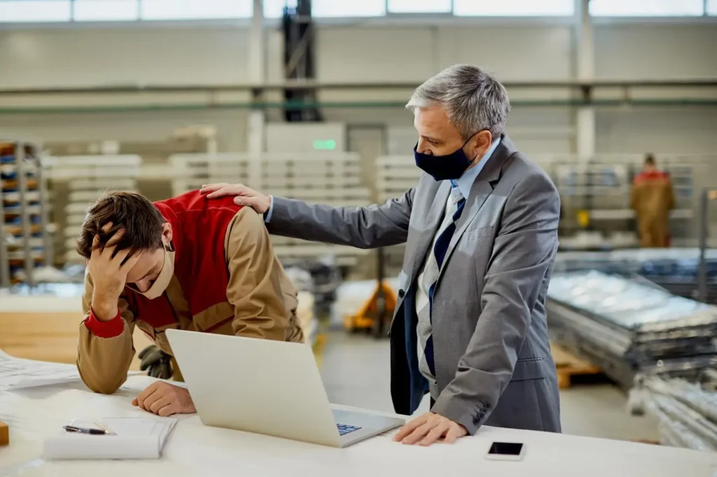 Businessman in suit comforting distressed worker at desk with laptop, emphasizing support in challenging situations.