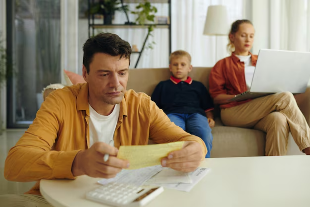 Man reviewing documents with a calculator, concerned expression, while a boy sits nearby and a woman works on a laptop, reflecting family law issues and appeals.