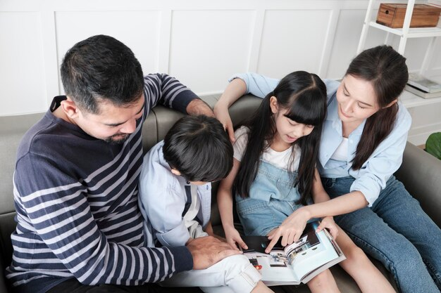 Family engaged in quality time, reading a book together on a sofa, emphasizing family bonding and support in a cozy home environment.